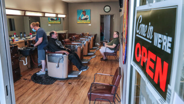 Barber and owner of Chris Edwards, left, wears a mask and cuts the hair of customer at Peachtree Battle Barber Shop in Atlanta