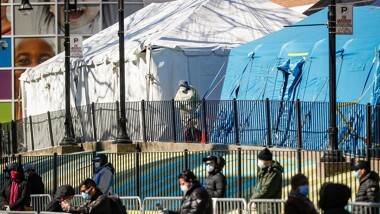 A medical worker standing between two medical tents with a crowd of people lined up 