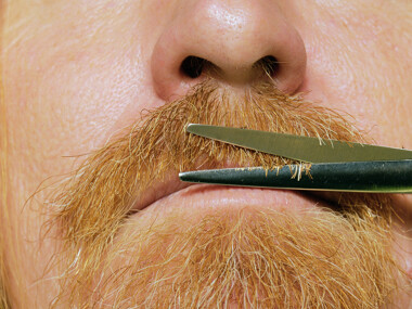 A closeup photo of a person trimming their beard with scissors