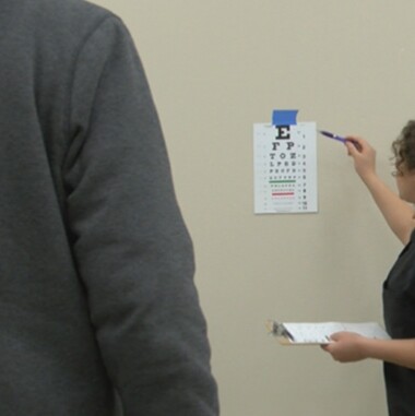 eye specialist conducting an exam with larger to smaller letters on a wall