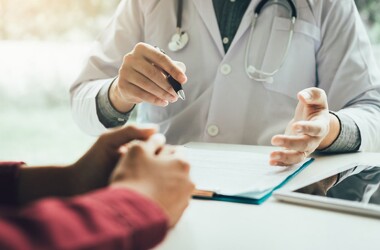 Person in a lab coat gesturing toward another person while both seated