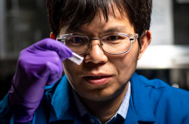 Researcher in lab looking at vial.