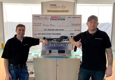 two men holding award check in front of invention display