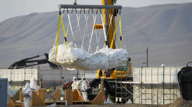 crane lifting covered materials while workers watch in haz-mat suits