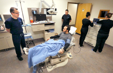 Man seated in dental chair with doctor and assistants around him
