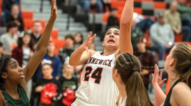 woman playing basketball and going for a lay up with a player behind and in front of her 