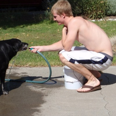 Young man letting dog drink from hose outside