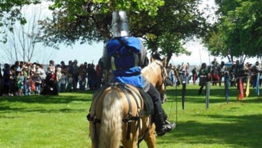 Person dressed in knights garb on a horse in a park