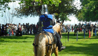 person in knights garb riding a horse in a park