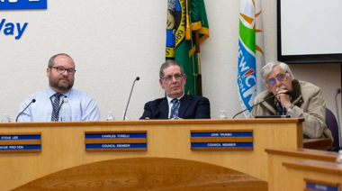 three men sitting behind council table