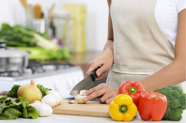 person in white apron chopping vegetables in their home kitchen