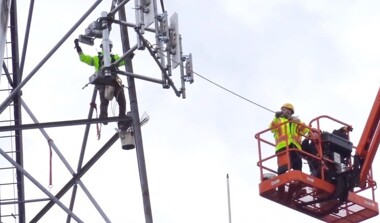 A worker on a lift near, and a worker on, a transmission tower