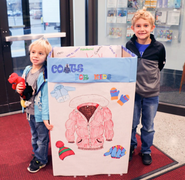 two kids in front of a coat bin