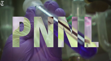 PNNL lettering in front of gloved hand holding glass tube