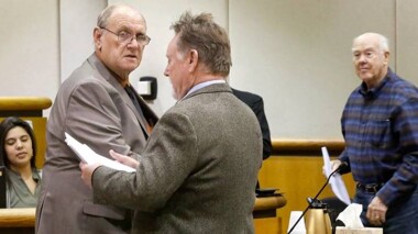 Bob Thompson looking over paperwork in a court room with other people surrounding