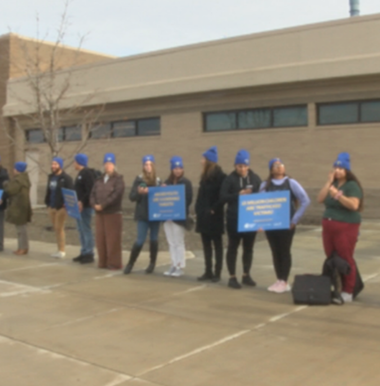 CBC students standing in a line wearing blue beanies and holding signs