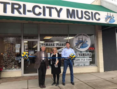 Three people cutting blue ribbon in front of Tri-City Music building