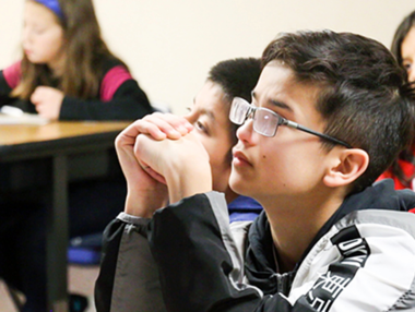 young student with glasses in a classroom looking up to the front