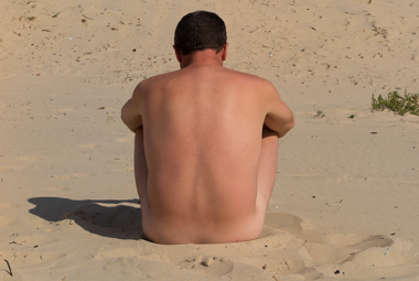 nude man sitting on a beach facing away fom the camera