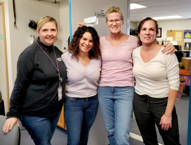 Four woman in a school office hold checks for the Super Hero Lunch Fund