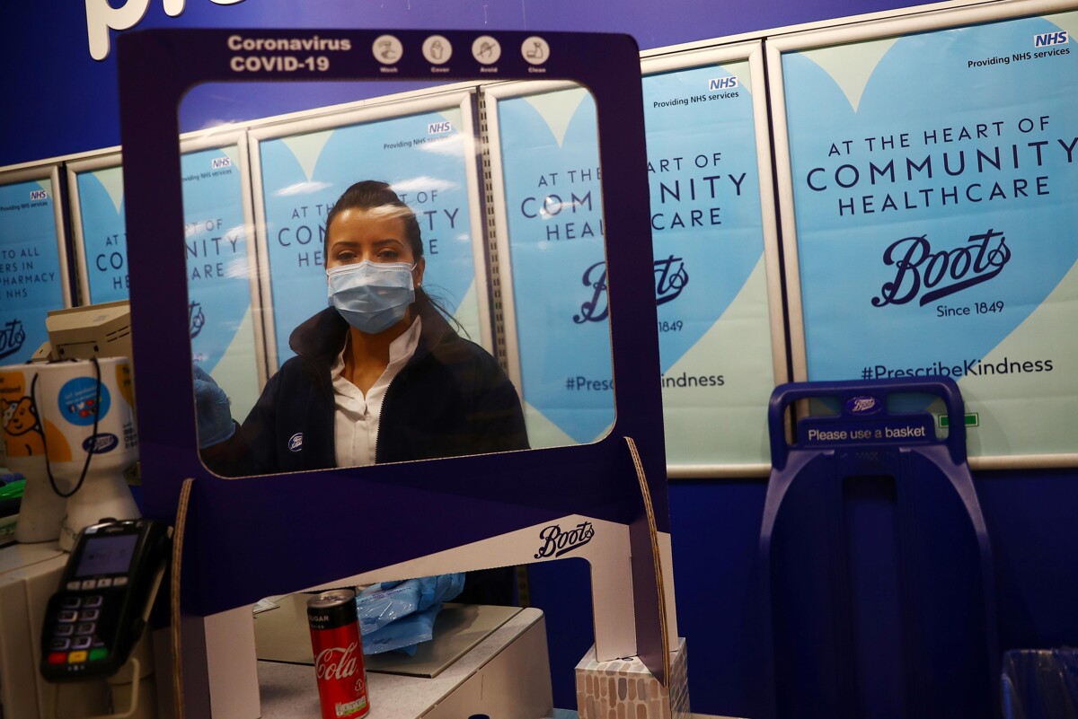 A Boots employee wearing a face mask, standing behind a protective screen at a checkout stand in London