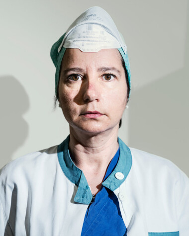 Monica Faloochi, a head nurse wearing scrubs with a mask pulled up to the top of her head
