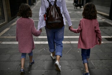A woman holding a hand of each of her two children while walking down the street